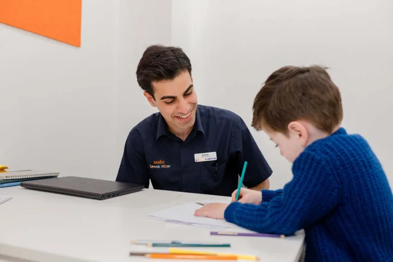 A child writing on paper during a speech therapy session at South Australia Speech and Hearing Centre, guided by a speech pathologist