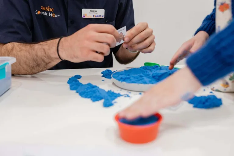 A child receiving speech therapy through play with kinetic sand at South Australia Speech and Hearing Centre, guided by a speech pathologist