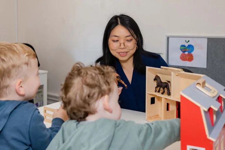 Two children playing with a toy house during speech therapy, guided by a speech pathologist at South Australia Speech and Hearing Centre
